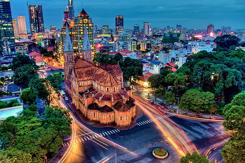 Notre-Dame Cathedral Basilica of Saigon at dusk, with the city skyline behind